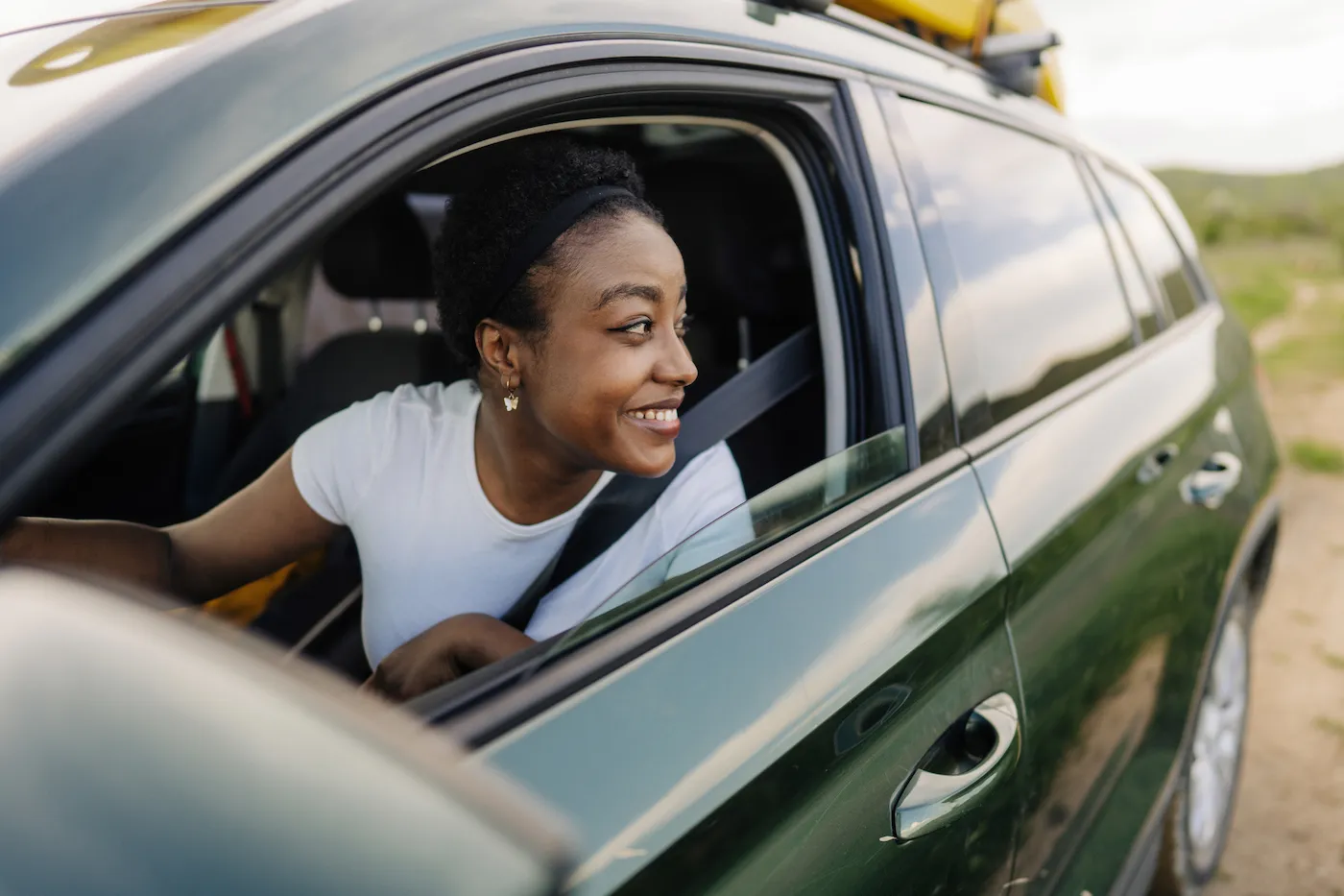 Photo of a young woman driving a car through nature and enjoying her local trip.