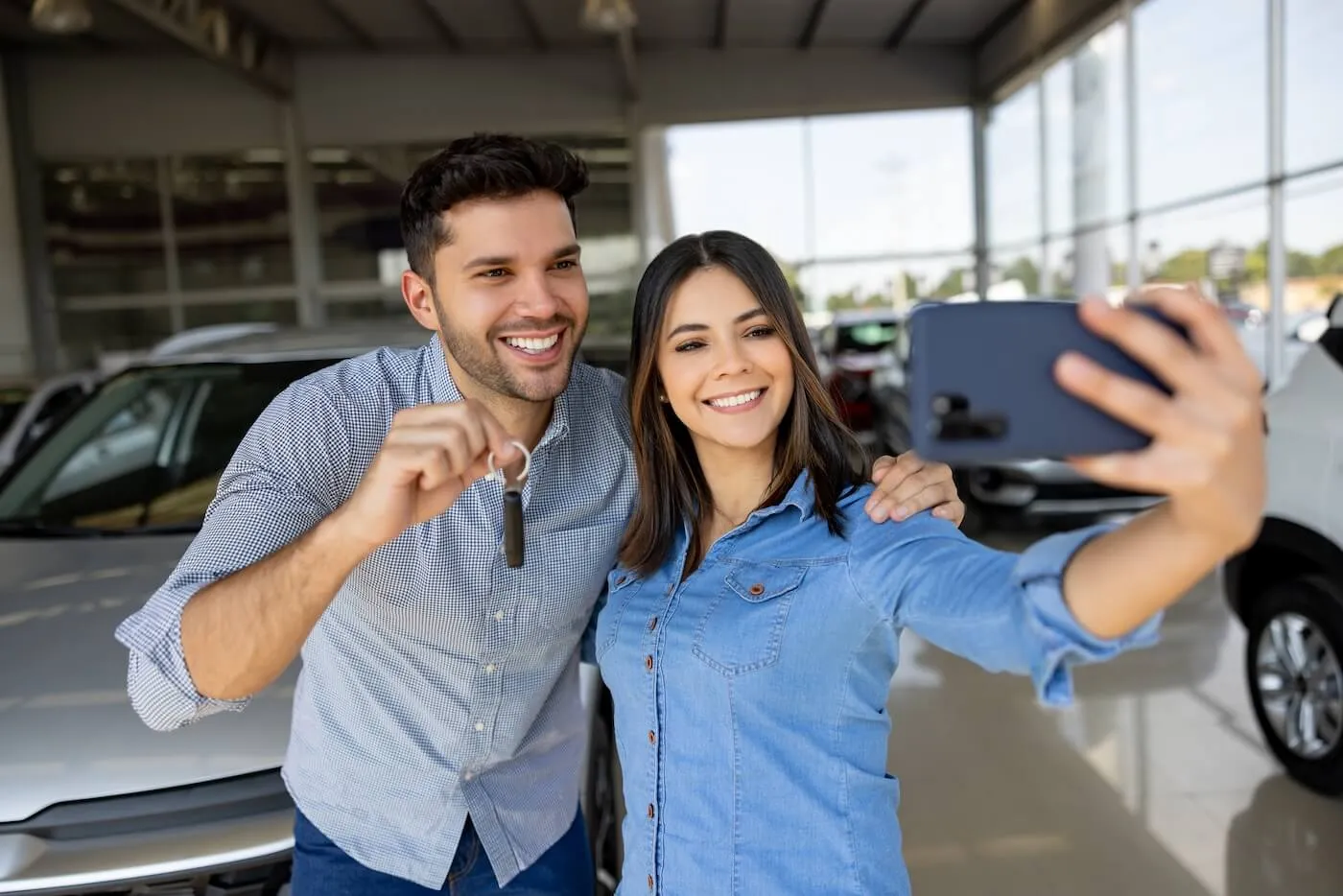 Smiling couple making selfie with the new car keys in the car dealership