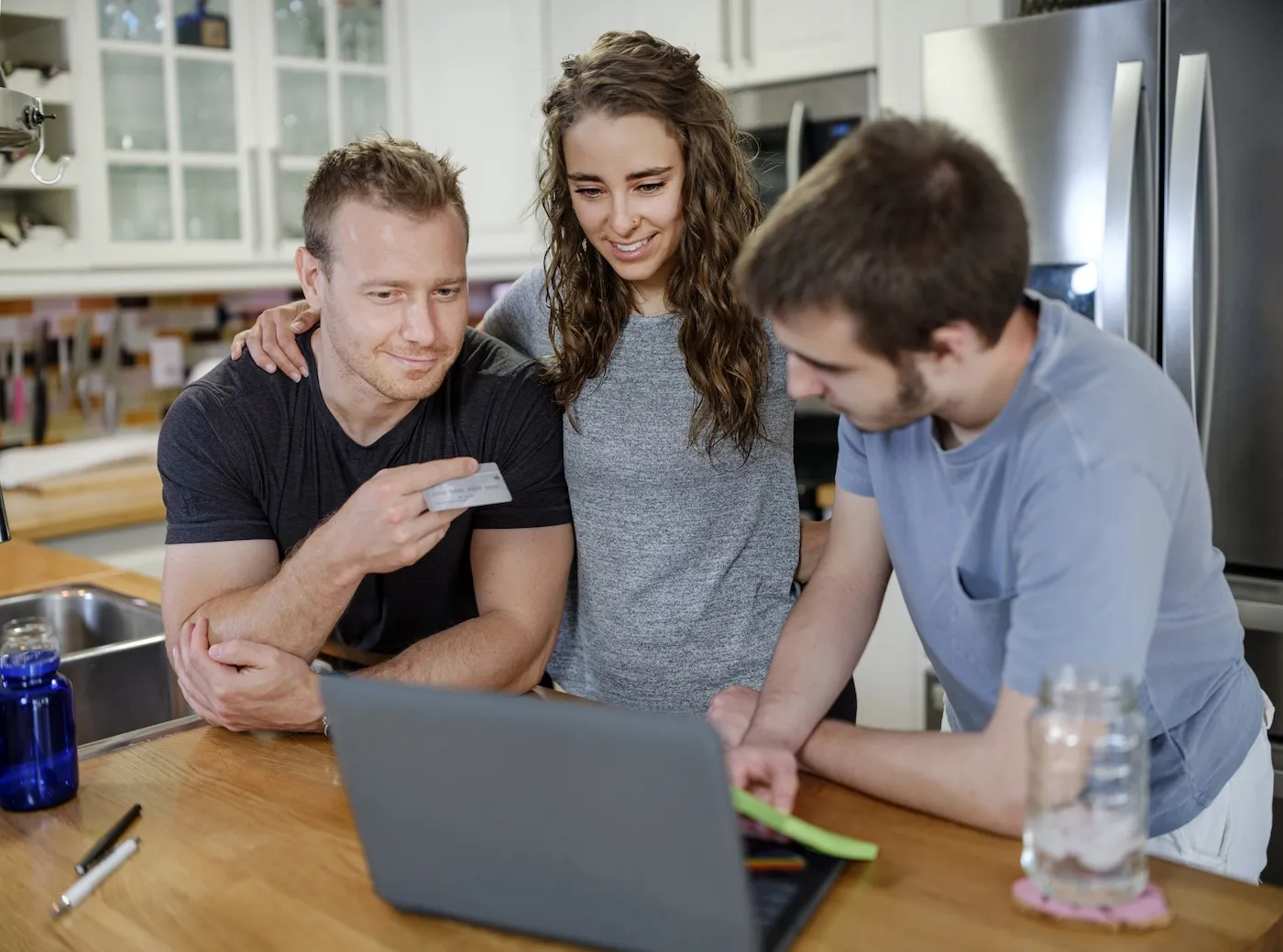 Group of people online shopping, standing in a kitchen with a laptop and a credit card.