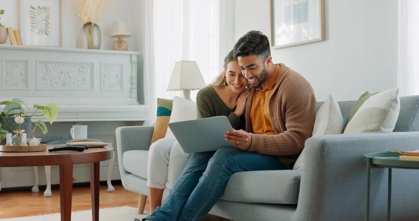 A man and a woman sitting together on their couch, using a laptop.