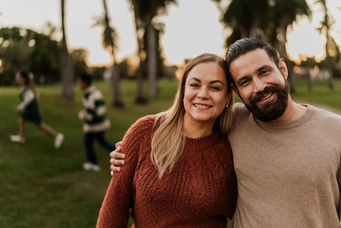 Smiling couple posing for a photo in the park, kids running on the background