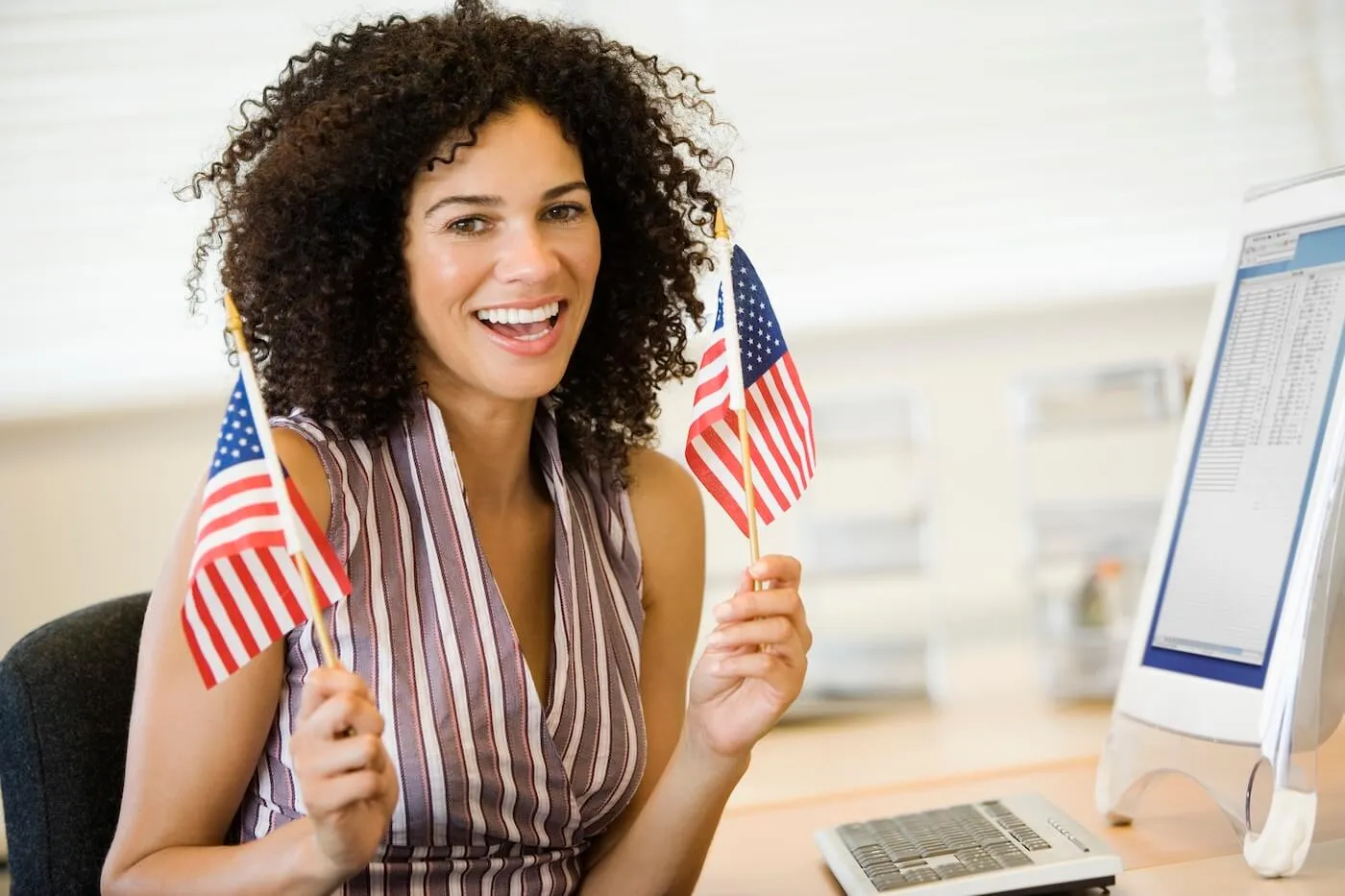 Smiling business woman waving American flags at her workplace