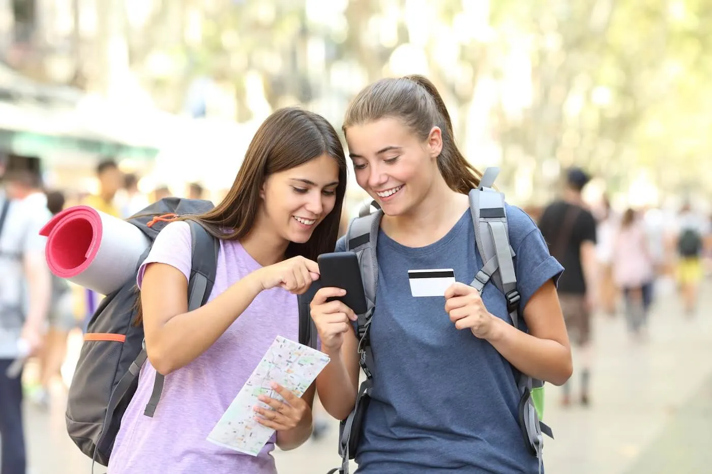 Two teenage backpacking girls use credit card to book a hostel via smartphone