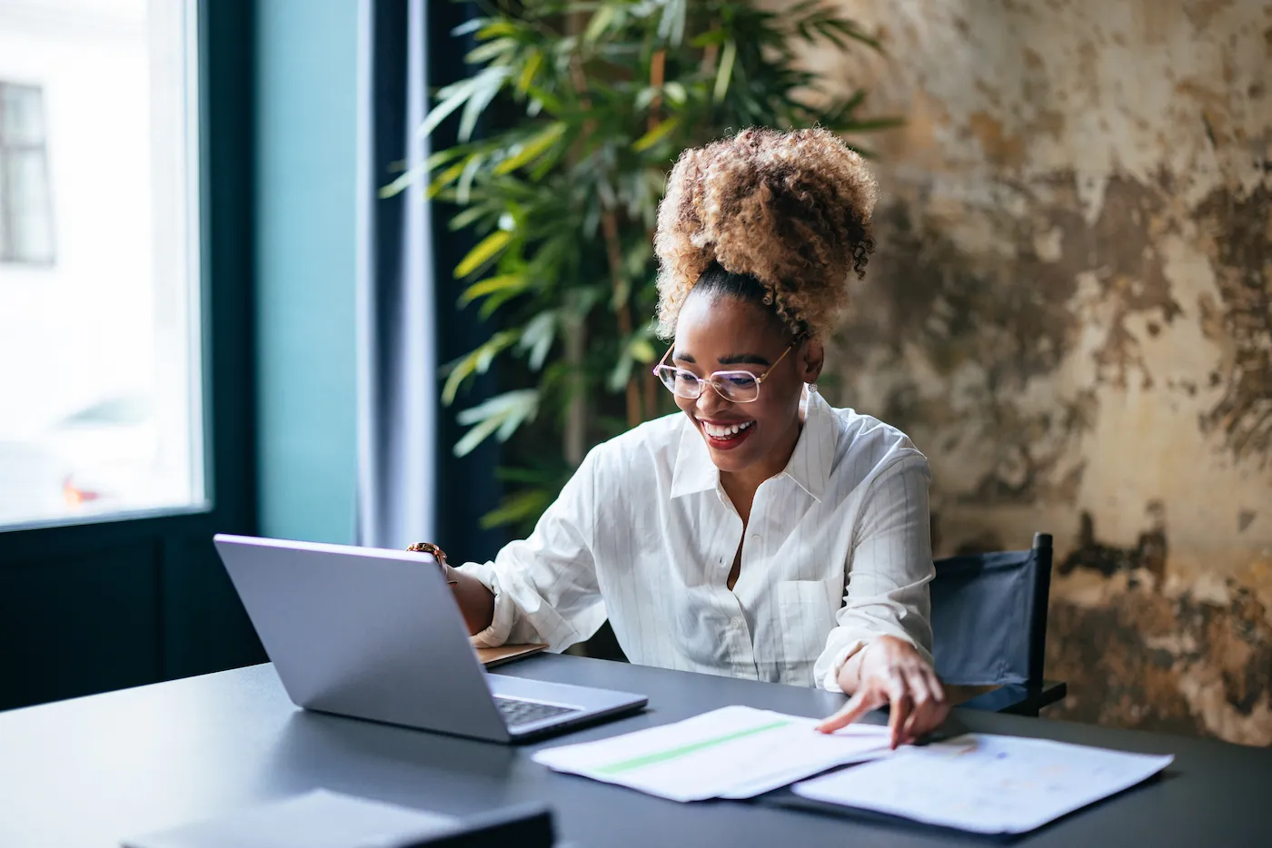 Smiling woman reading while sitting at office desk with her laptop.