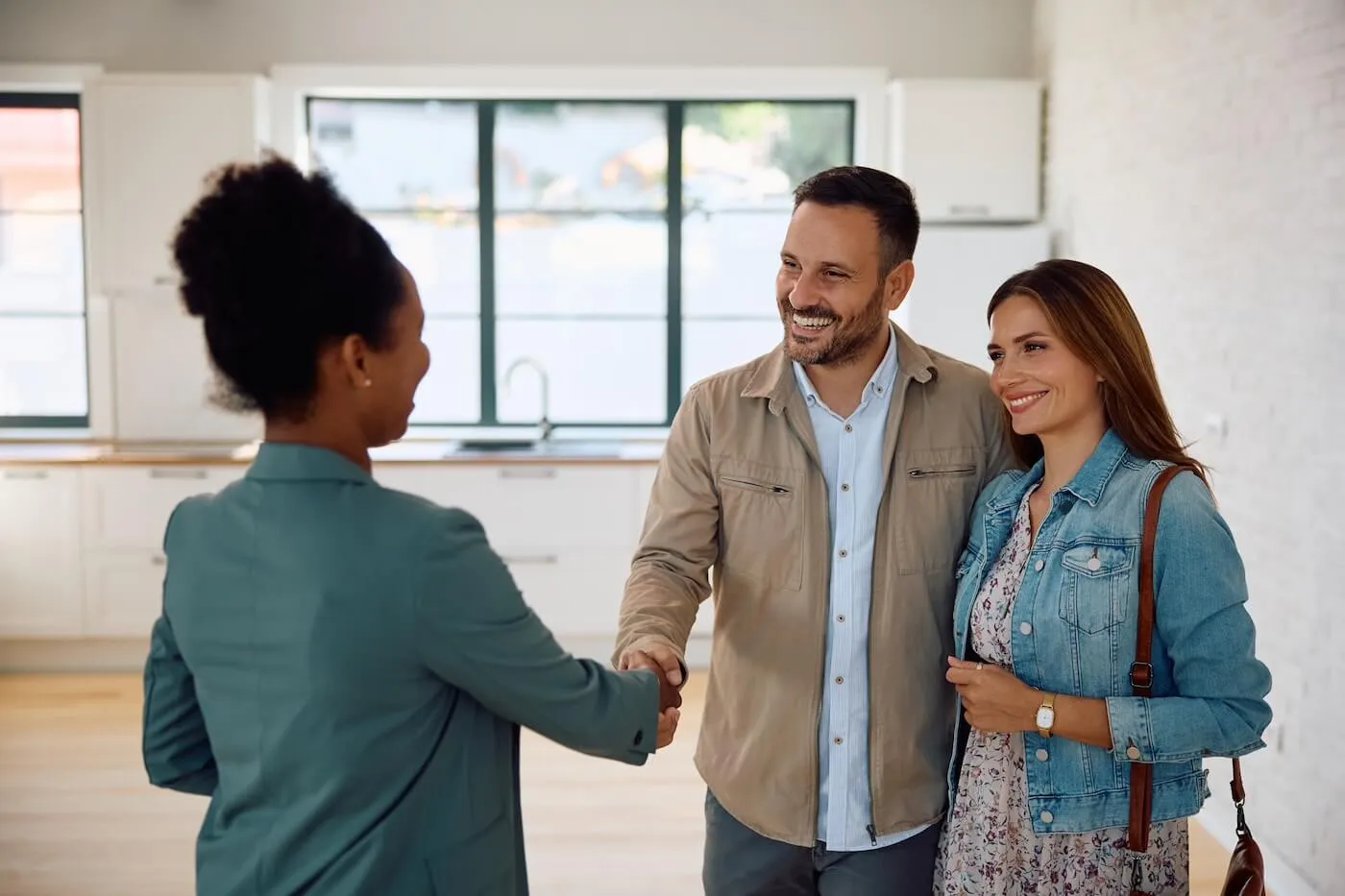 Young couple shaking hands with a female real estate agent in a new house