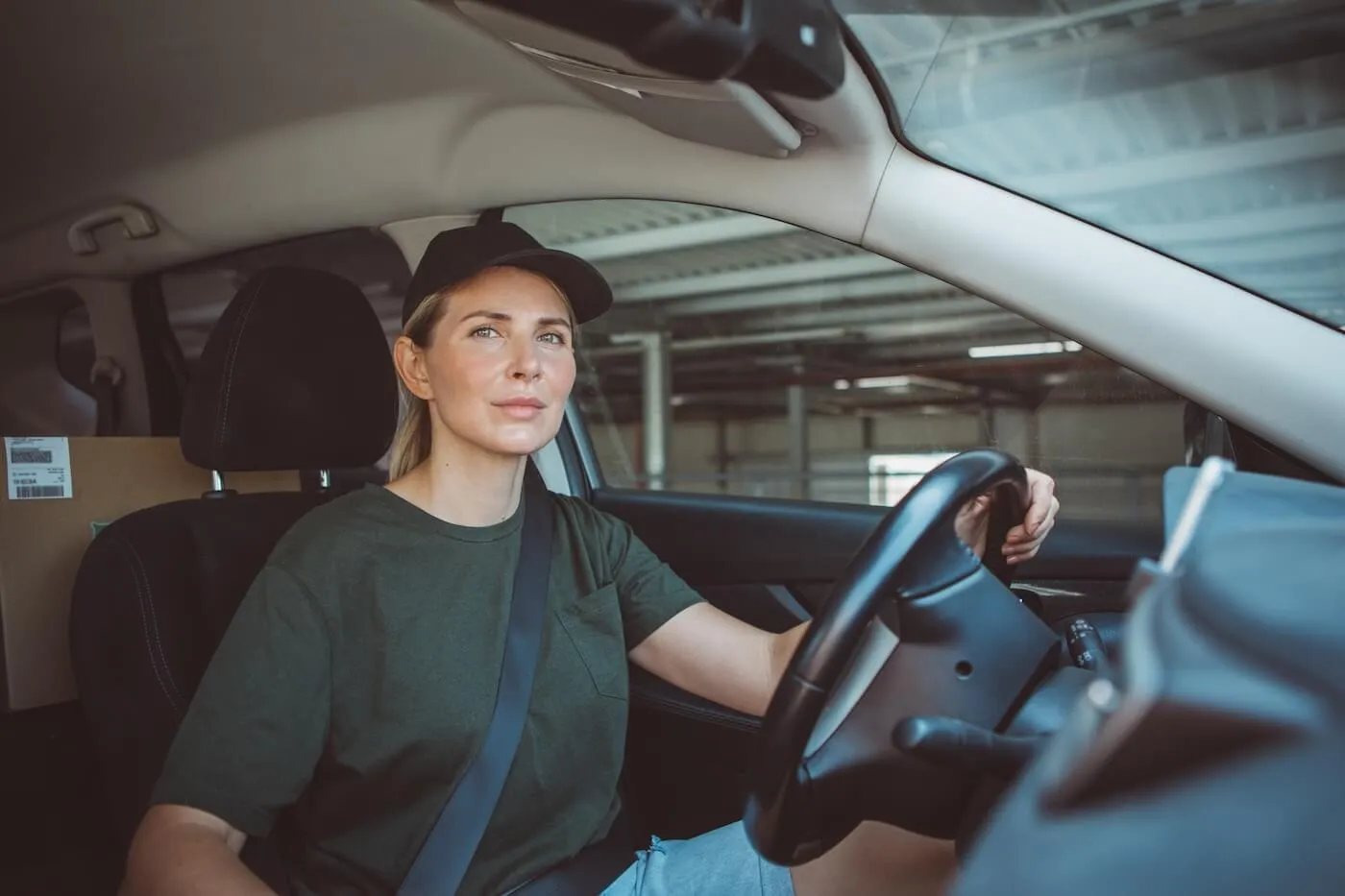 Woman in a baseball cap driving a car with a delivery box on the back seat