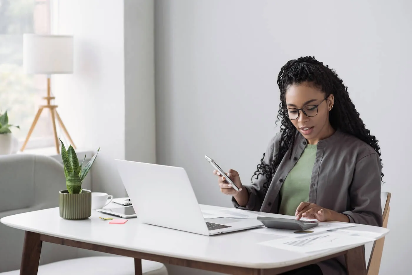 Woman using her laptop and calculator while holding a smartphone