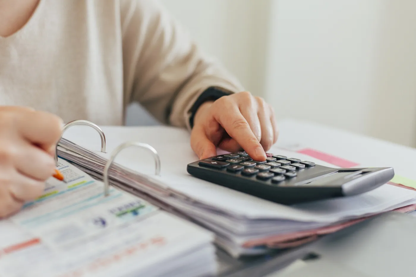 A person using a calculator to calculate their savings rate, writing it down in a financial planning binder.