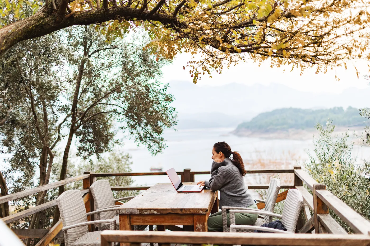 Woman working remote from sidewalk cafe next to ocean