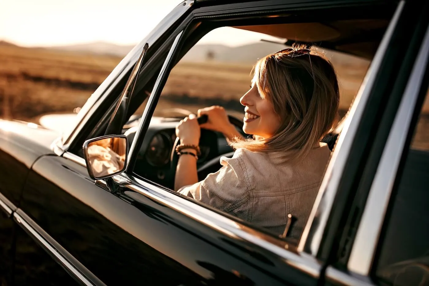 Smiling woman driving a classic car at sunset