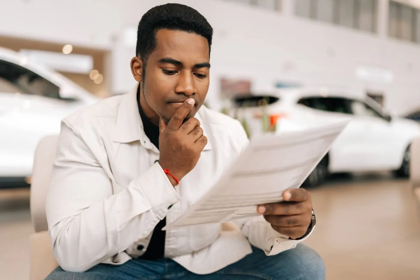 Pensive young man looking at printouts in the car dealership