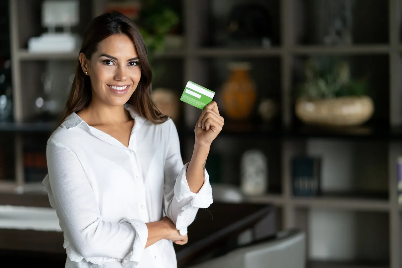 A woman at home holding a credit card and looking at the camera