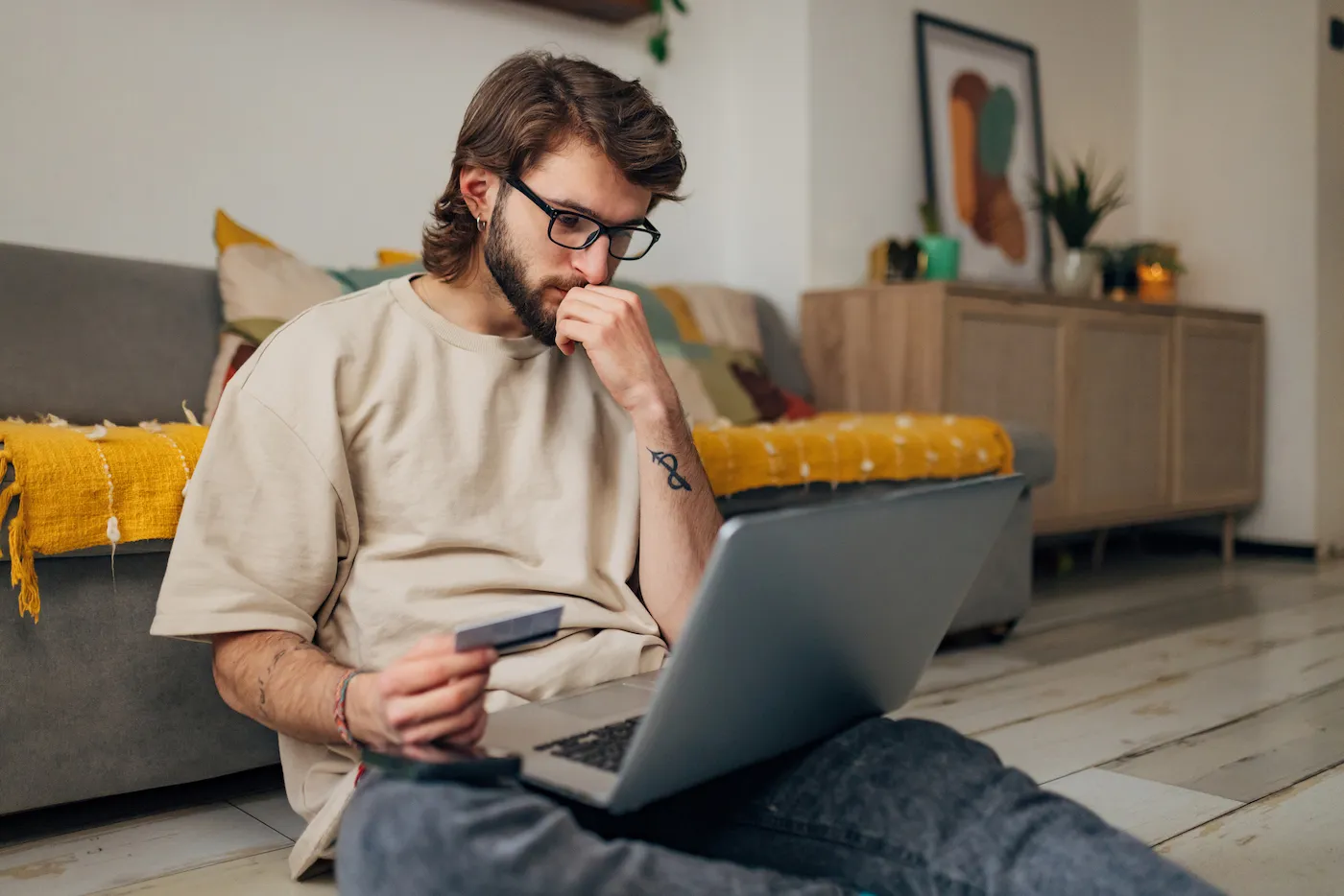 A man looking at his laptop with concern, holding a credit card.