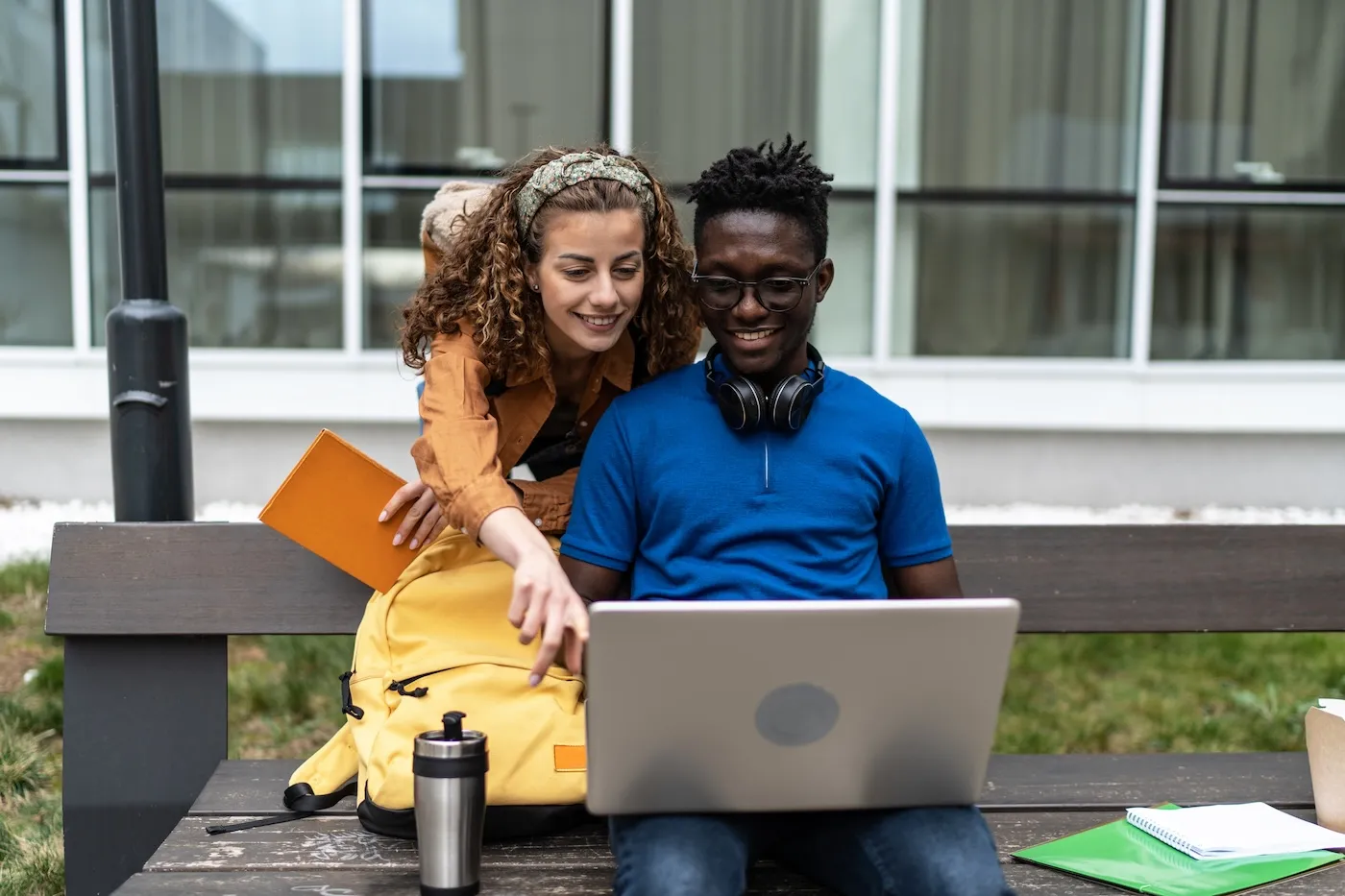 Two friends sitting outdoors and using laptop.