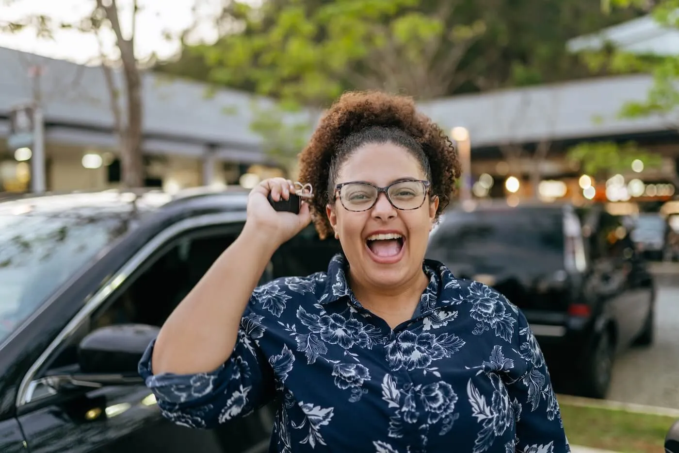 Photo of a happy woman holding car keys, the black cars are parked on the background