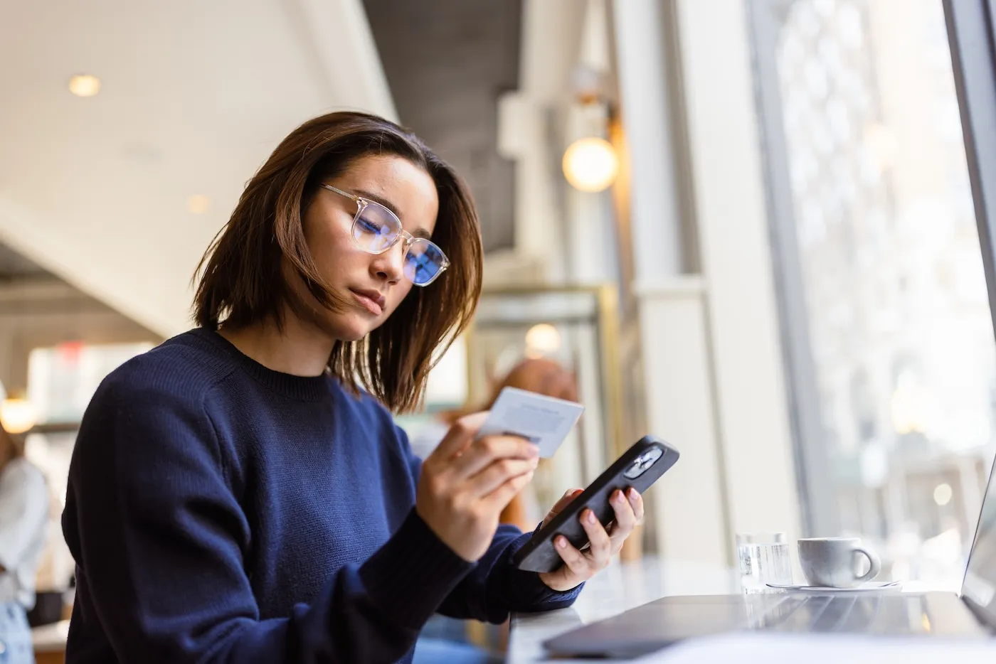 A woman using a balance transfer card and her phone in a cafe.