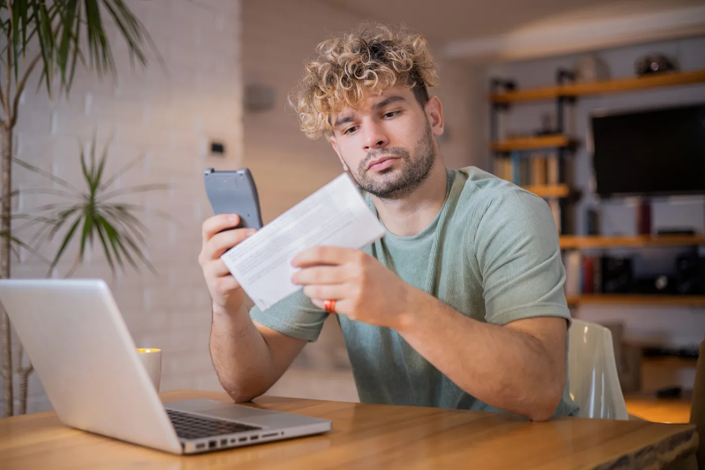 Man trying to roll over unused 529 funds. Sitting at a desk holding a paper and a calculator in front of a laptop.