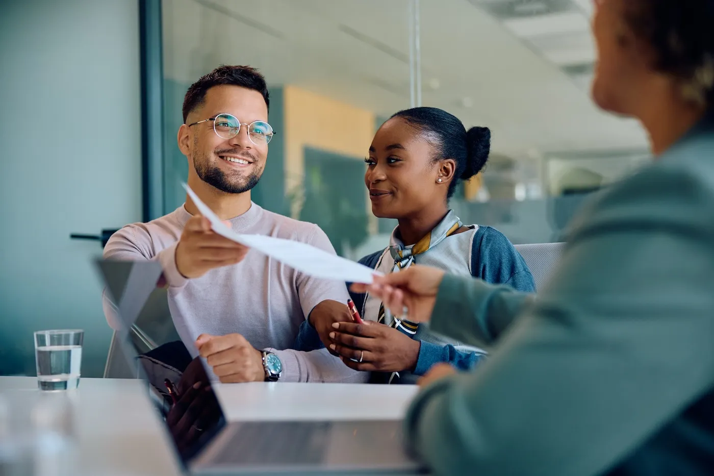 Happy man and woman handing over paperwork to their mortgage manager in the office.