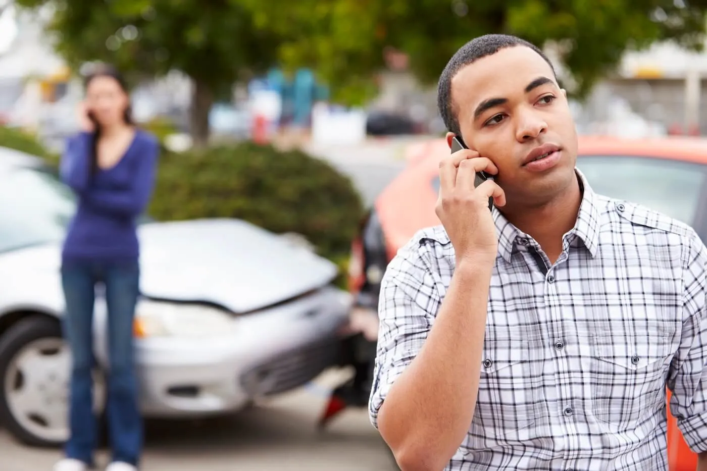 Man is calling the insurance company after the road accident. A female driver on the background is also making a phone call