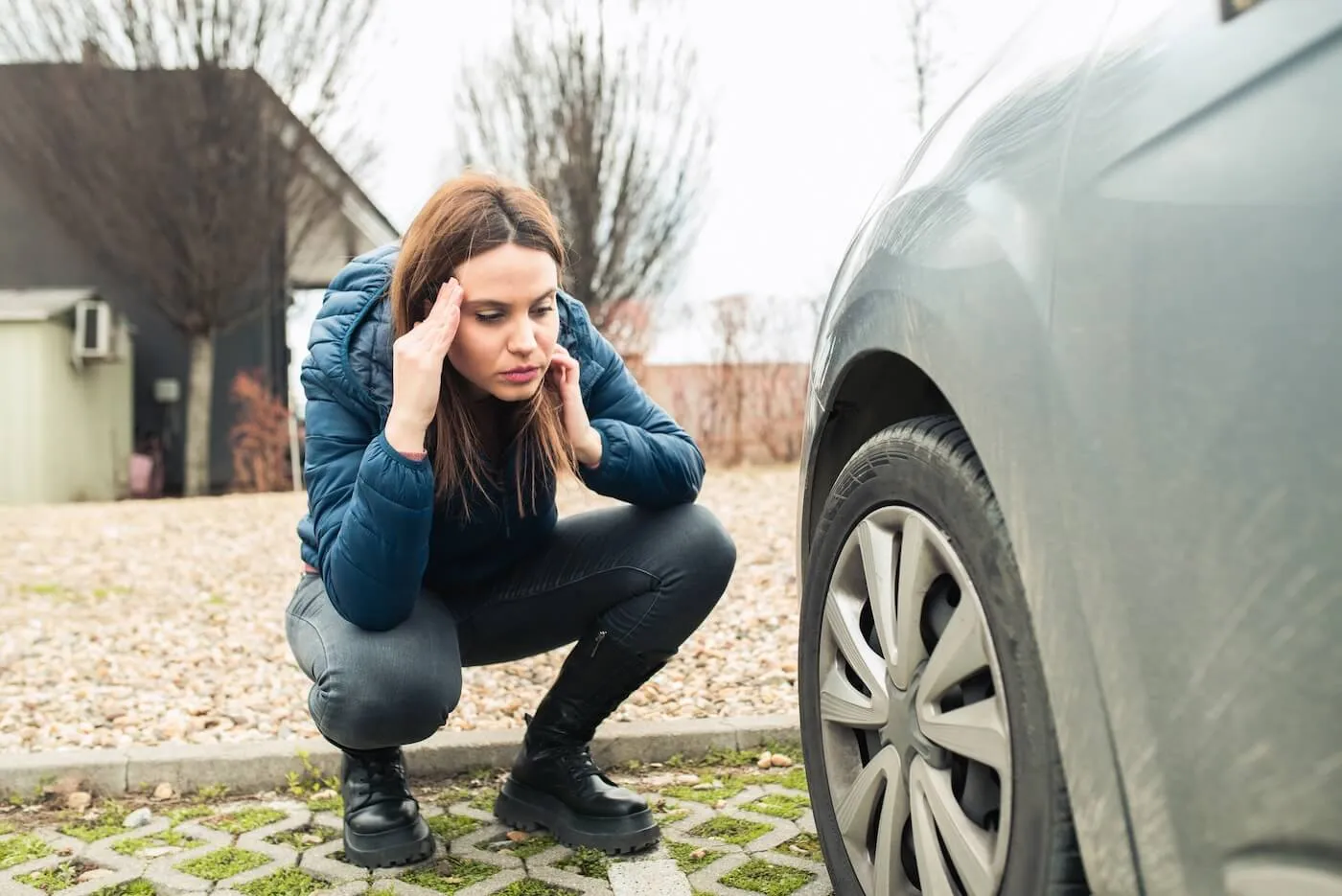 Concerned young woman looking at the flat tire of her vehicle that is parked on the street