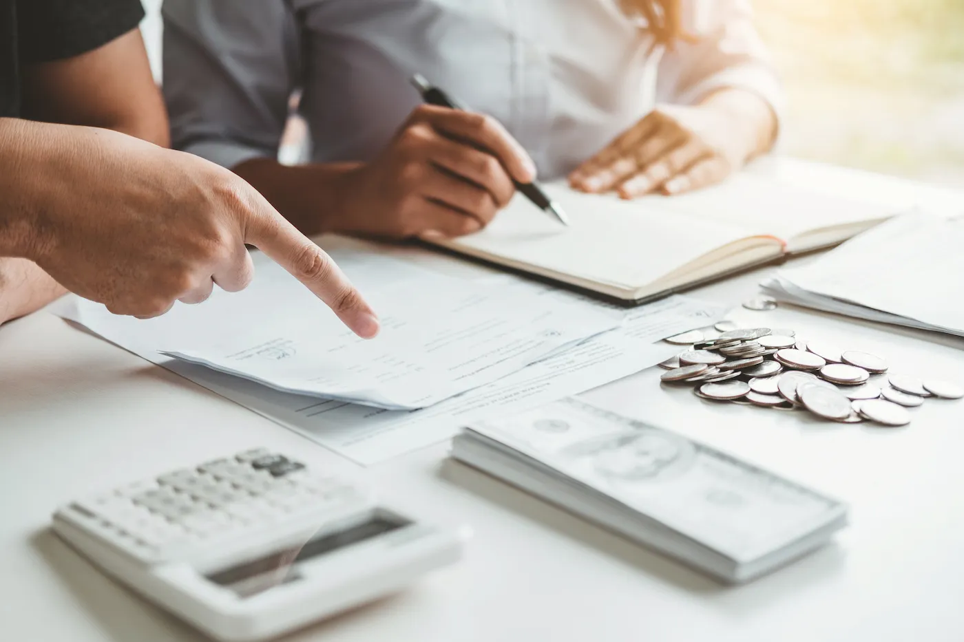 Two people working on a cash management account at a desk with. a notepad, cash and a calculator.