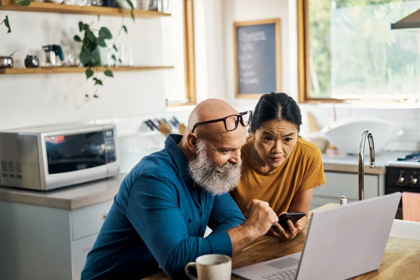 Mature couple are comparing car insurance options on their laptop in the kitchen