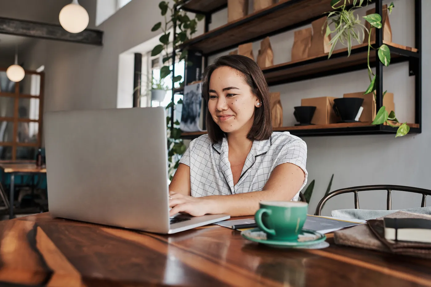 Shot of a young woman using a laptop in a cafe to check her checking and savings accounts.