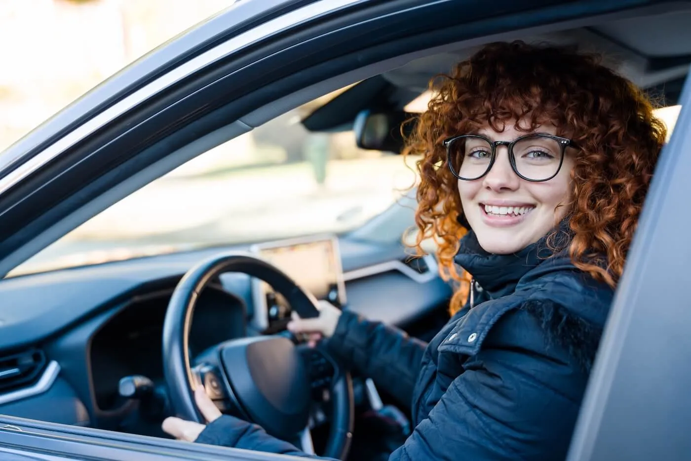 Smiling young woman in glasses driving a car