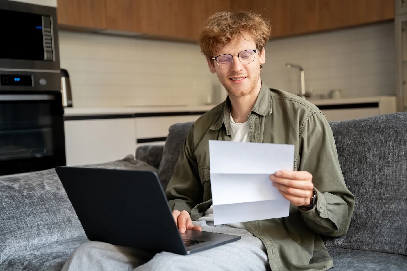 Young college student filling out the FAFSA with divorced parents, sitting on the couch holding papers with a laptop.