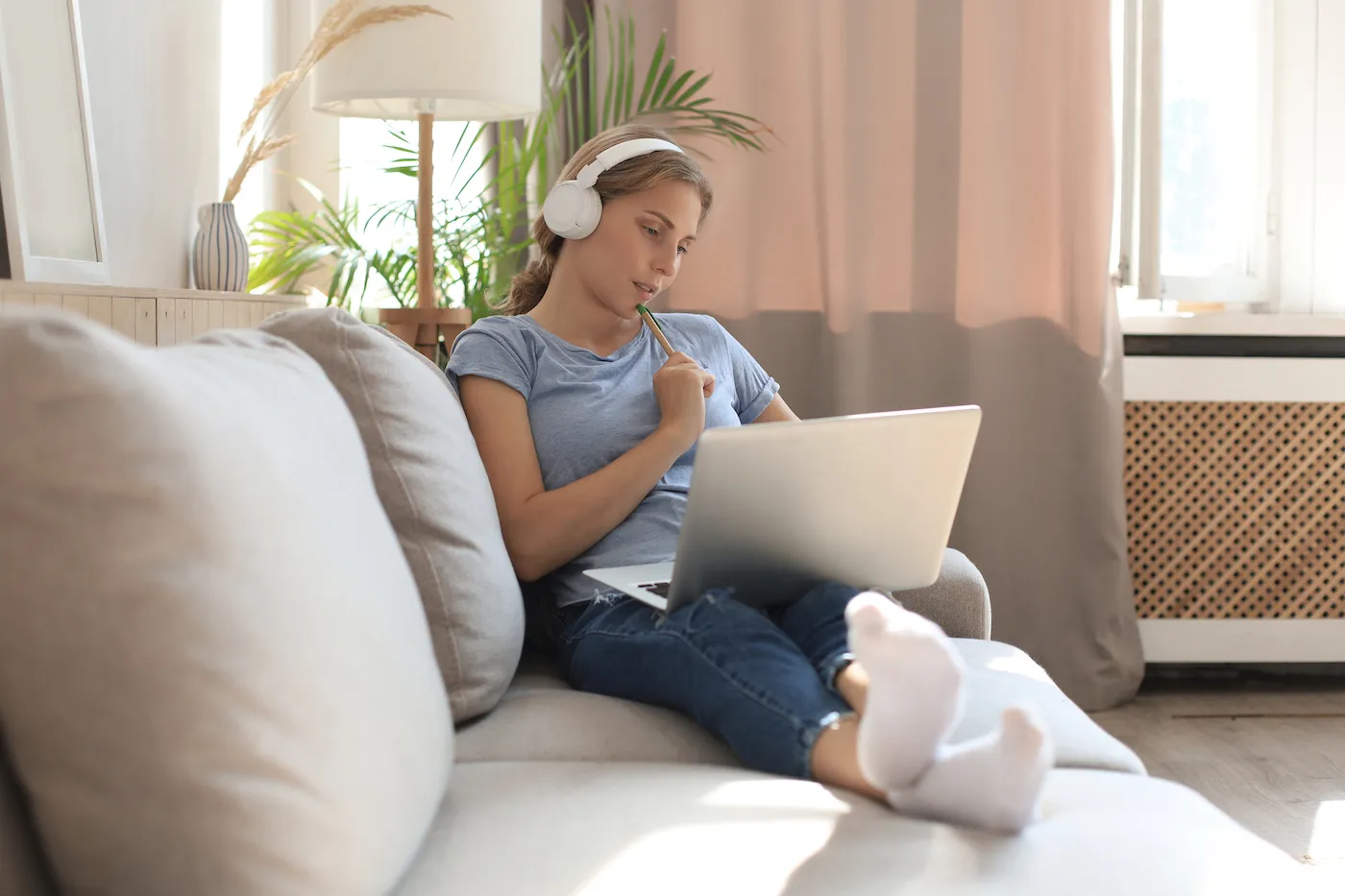 Smiling young college student with headphones and laptop on the sofa learning how to invest in a 529 account for herself.