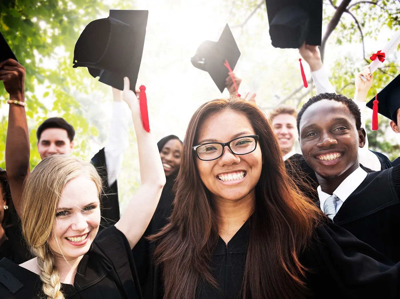 A group of happy smiling college students in caps and gowns celebrating their graduation.