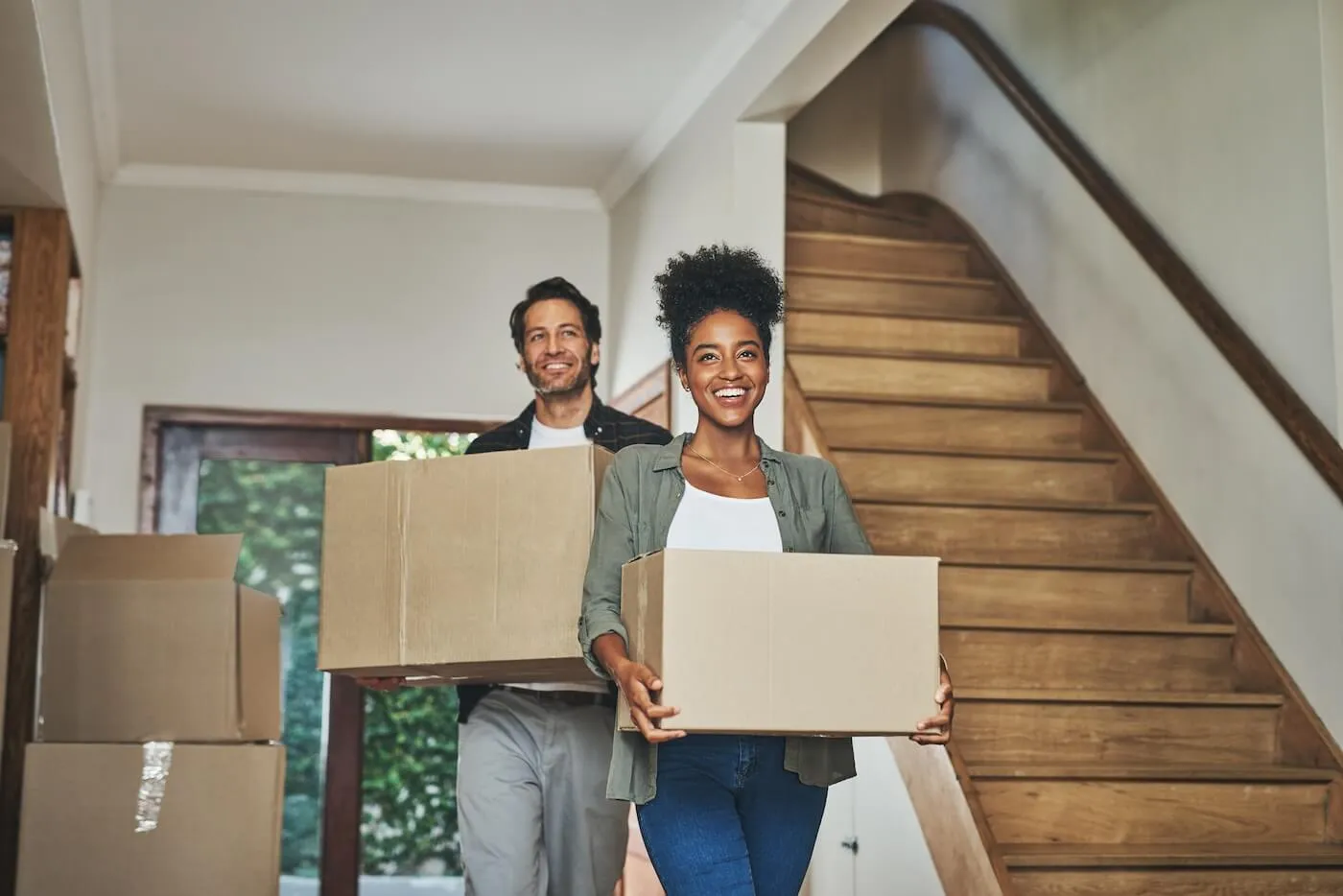 Smiling young couple carrying the moving boxes into the new house