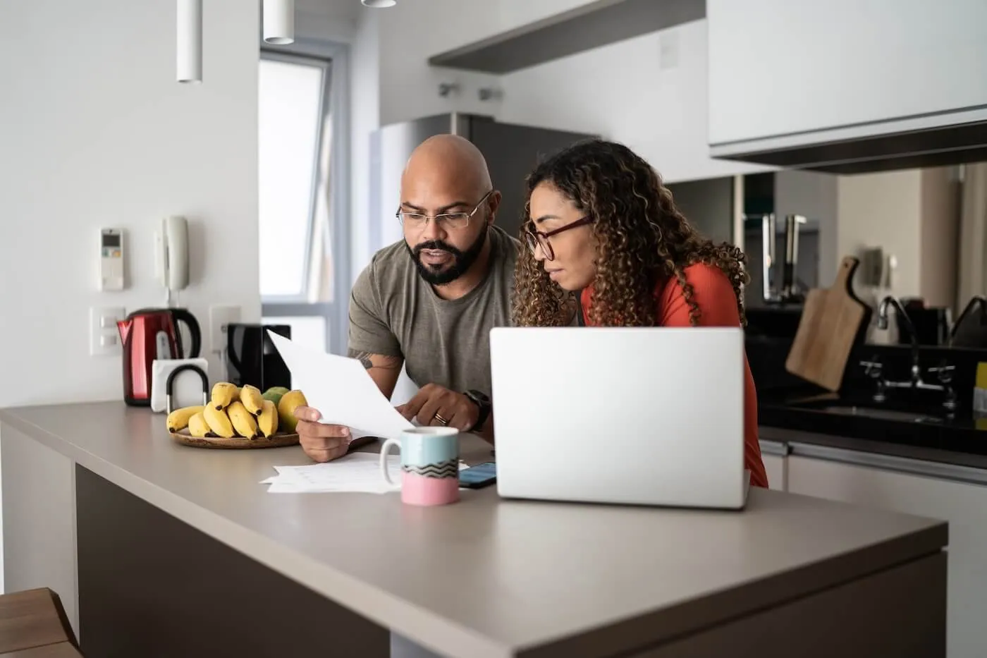 Focused couple reviewing their mail in the kitchen while using the laptop.