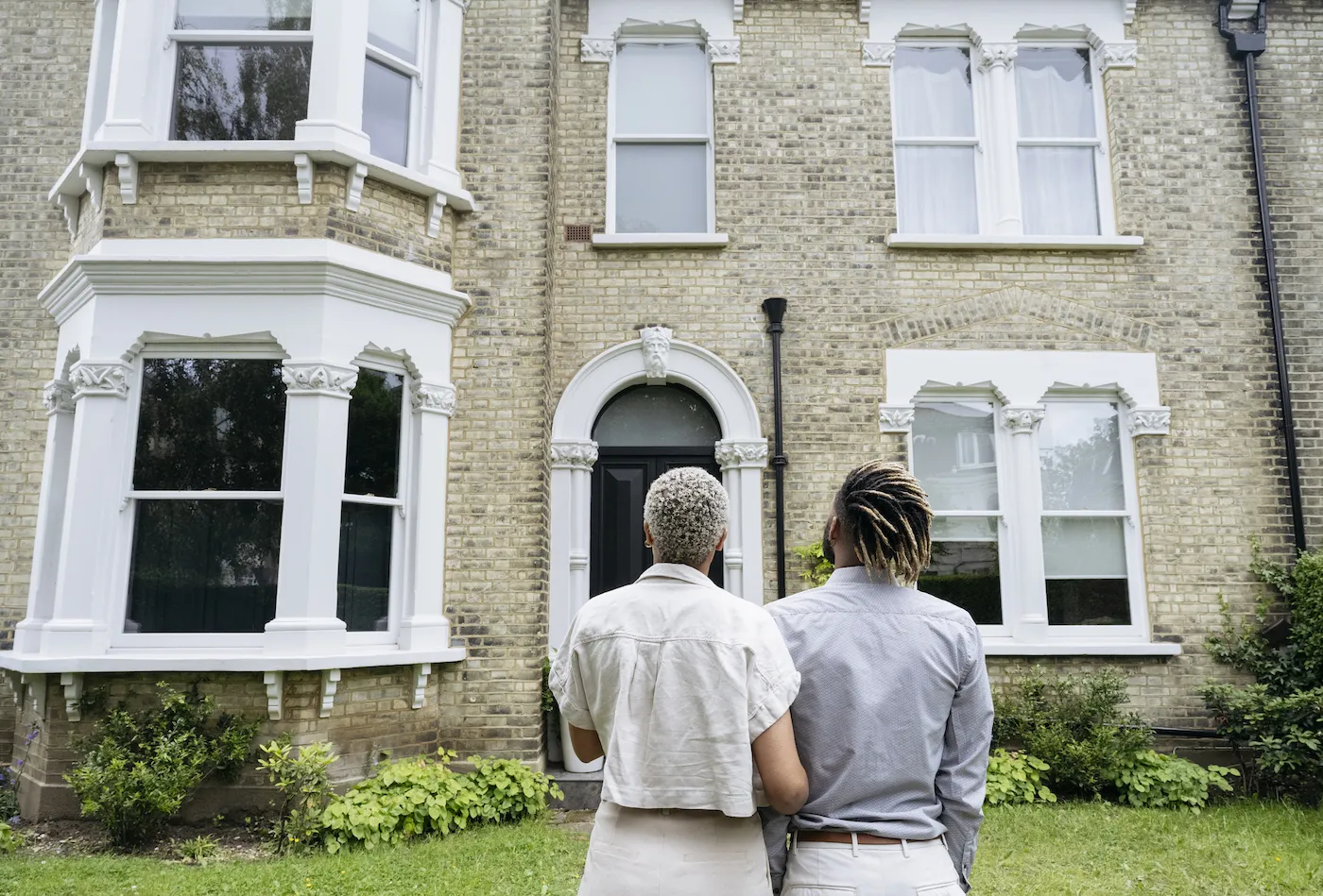 Rear view of couple standing arm in arm and looking at facade of restored 1890 double fronted Victorian house.