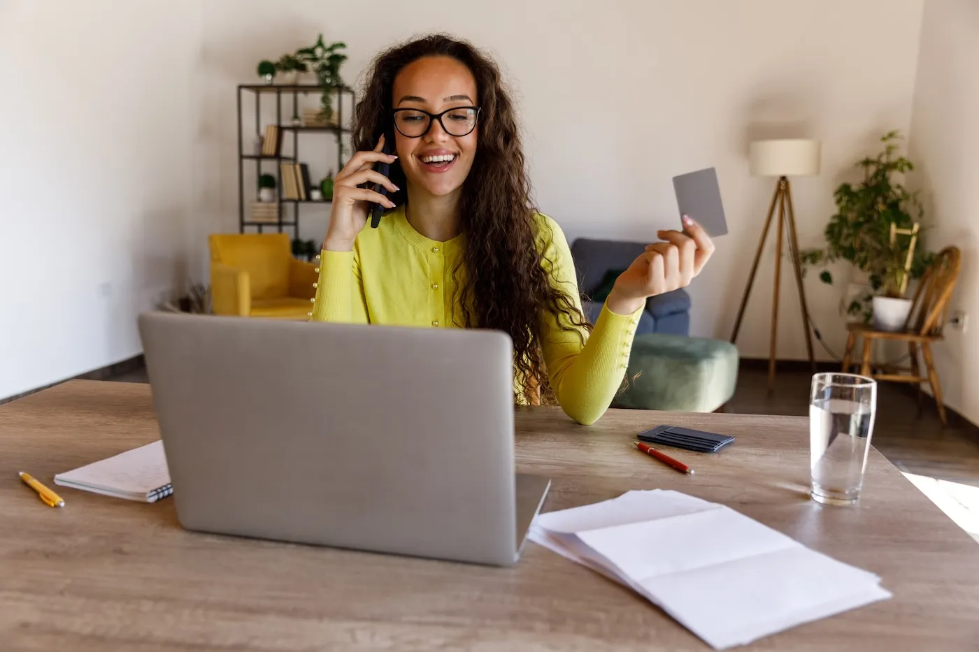 A smart young woman sitting at dining table, managing her home finances on laptop. She is holding a credit card.