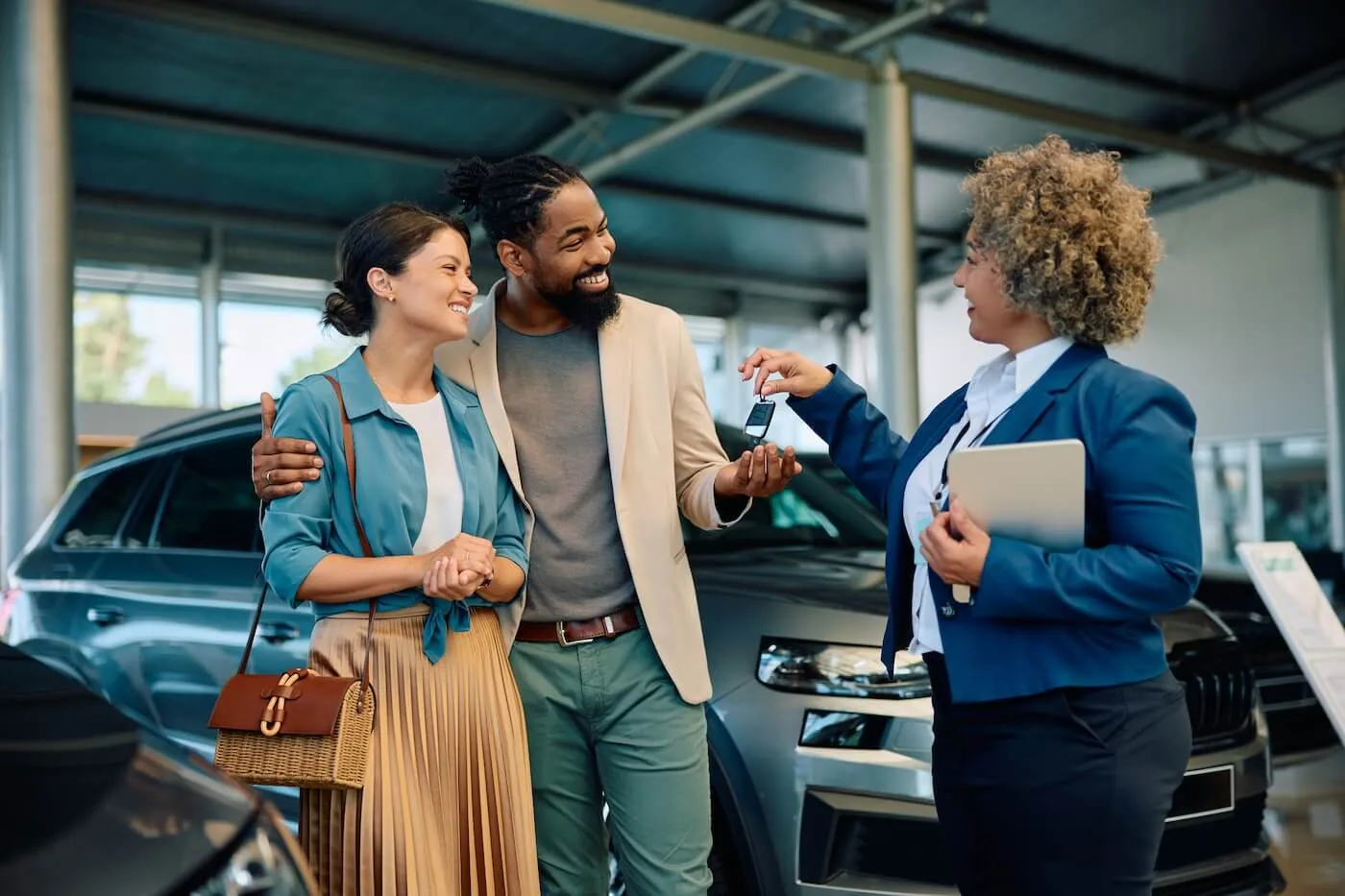 Happy young couple taking car keys from the female dealership agent