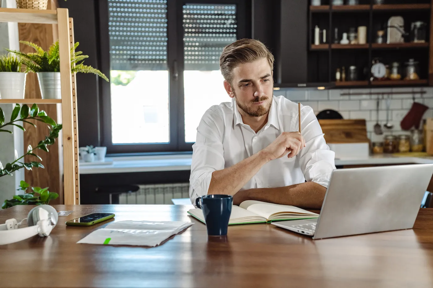 Young businessman in a white shirt sitting at the table and going through paperwork. Analyzing, planning, forecasting.