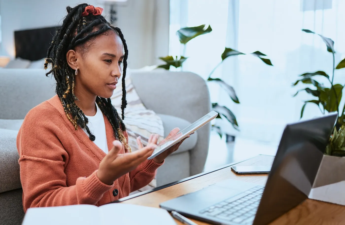 A woman using a tablet and a laptop to work on her finances while sitting at a table with papers on it.