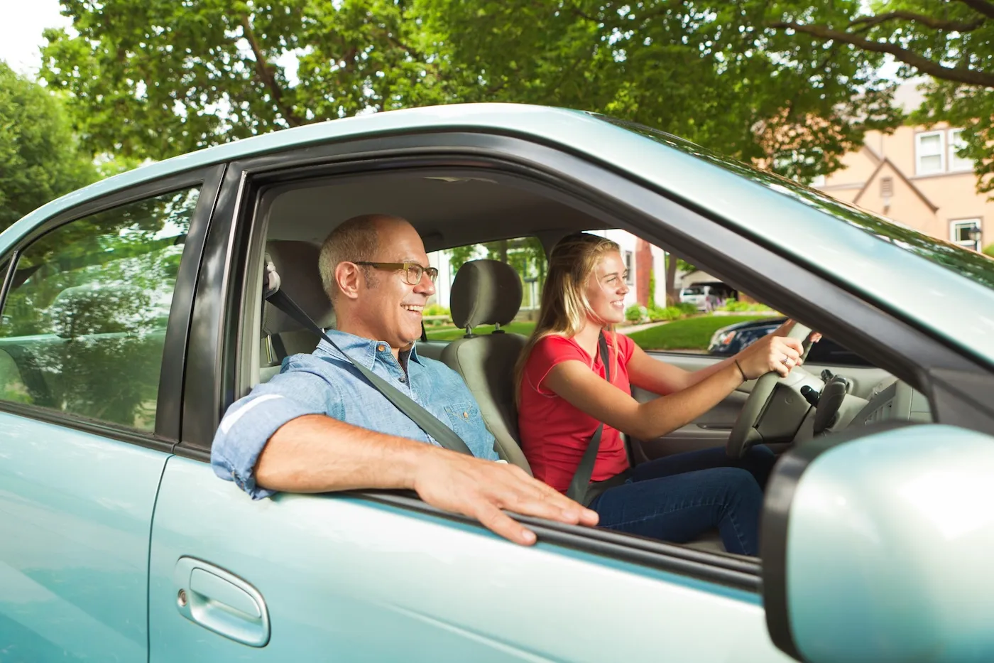 A happy young teenage girl learning to drive in a SUV. Her dad is in the passenger's seat.