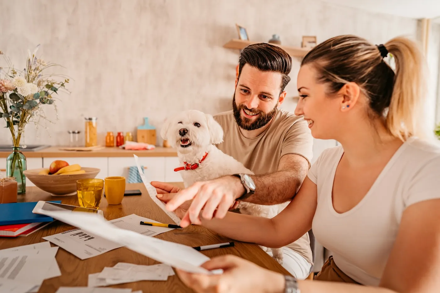 Young couple sitting in their living room and checking their finances. Man holding toy dog in his lap.