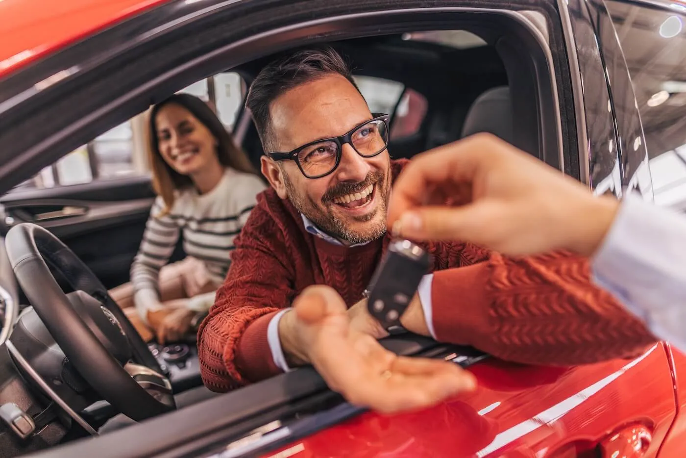 Happy couple sitting in a new car, the man taking the car keys from the seller