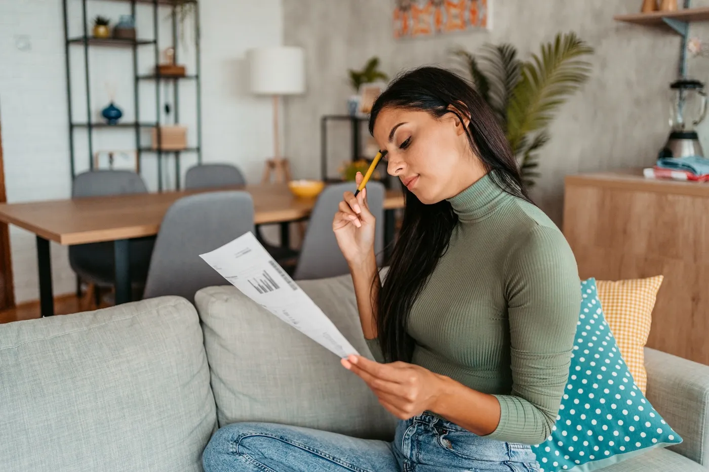 A young woman checking her finances while sitting on the sofa at home.