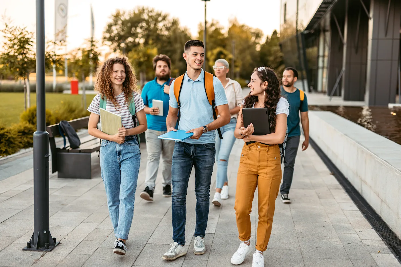 Group of friends walking on the university campus, holding books and notebooks.