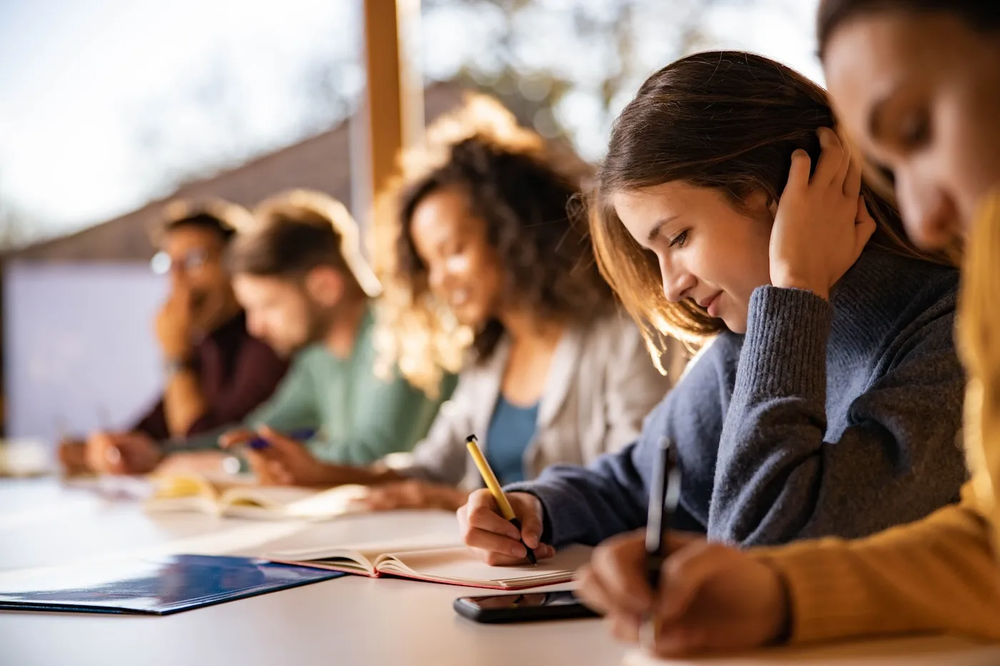 Smiling students writing an exam while attending a class at college classroom.