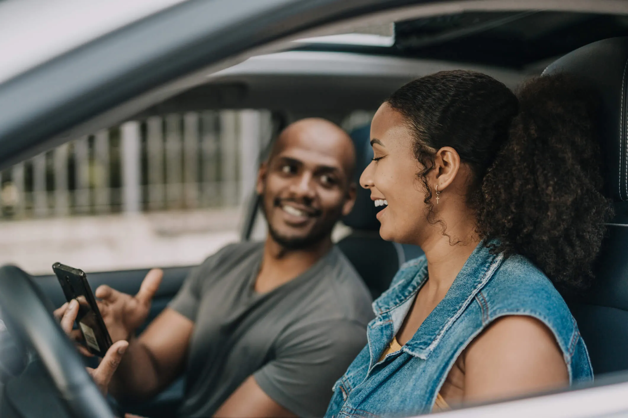 A smiling man in a car showing something to a female driver on his smartphone