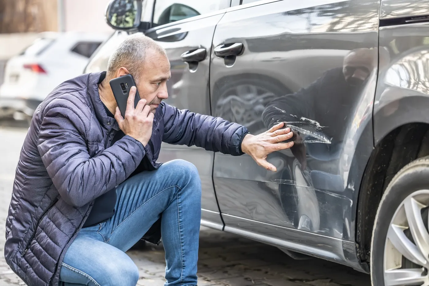 A man inspects damage to his car door as he calls the insurance company.