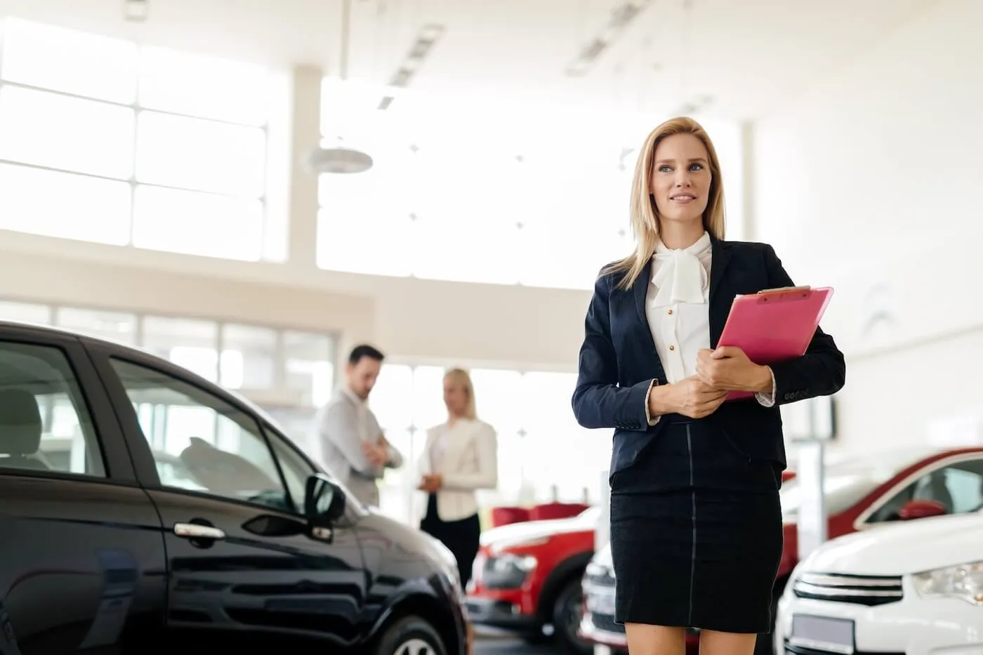 Female agent holding a folder in a car dealership, couple of customers on a background