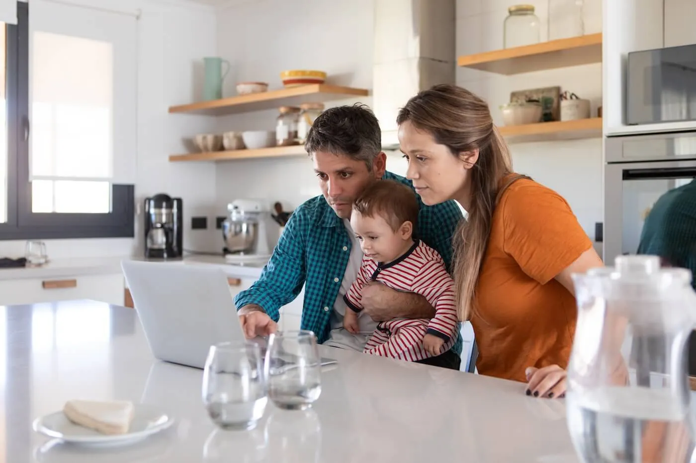 Young family of three using using a laptop in a kitchen