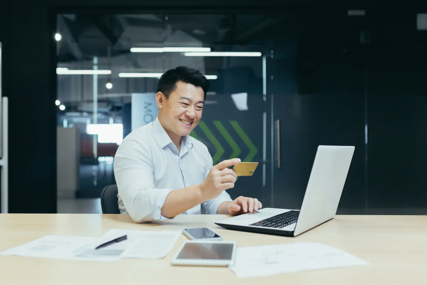 A man sitting at a table holding a credit card and using a laptop.