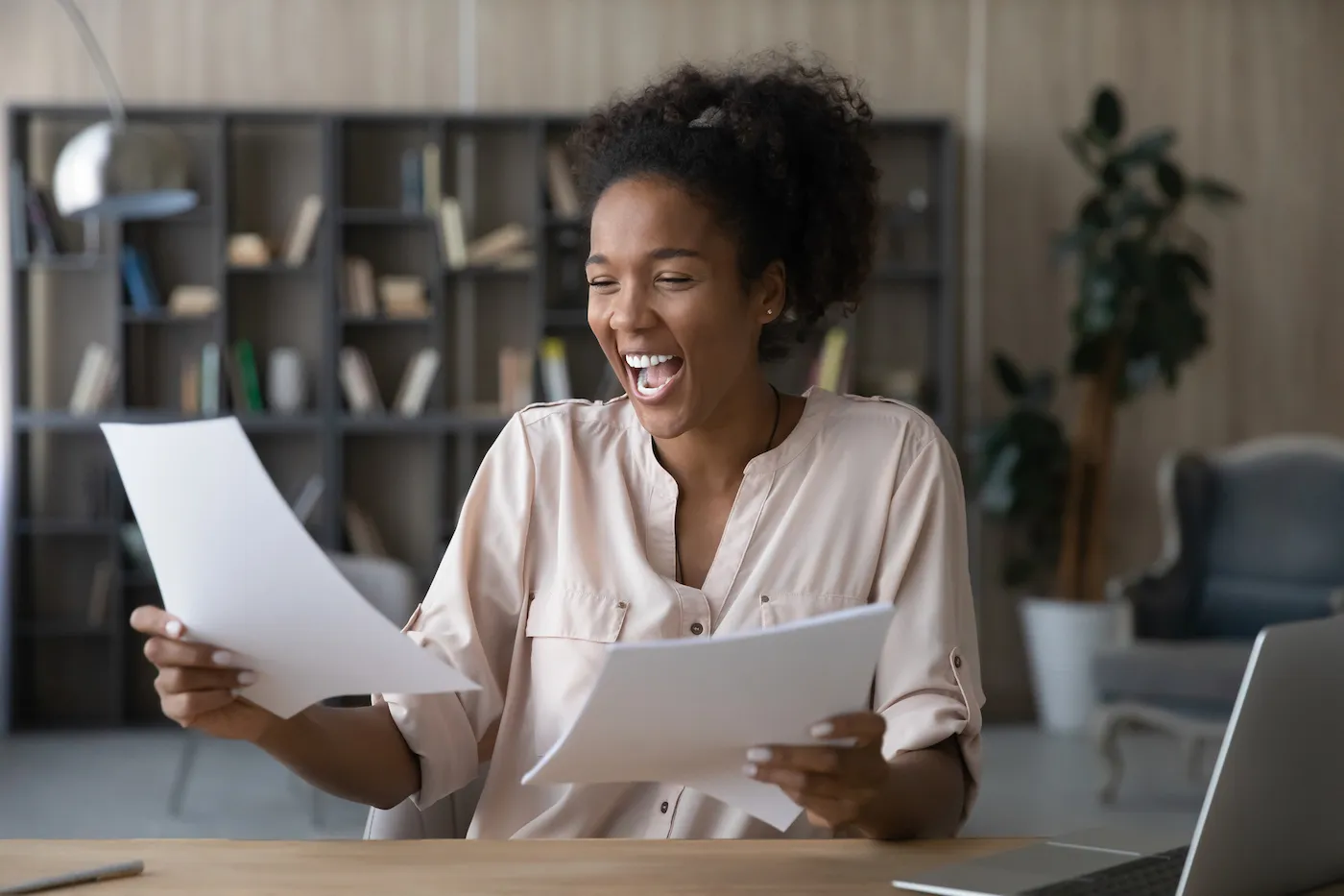 Happy young woman reads good news in a letter at her desk.